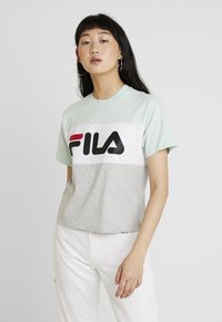 T-shirt coloré en blocs de menthe verte, blanche et grise avec un grand logo FILA noir. Manches courtes et coupe décontractée. Matière en coton doux.