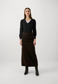 Zwart geribd lang mouwen top met een V-hals en een bruine denim maxi rok. De rok heeft een hoge taille en voorste naden. Gecombineerd met zwarte enkellaarsjes.