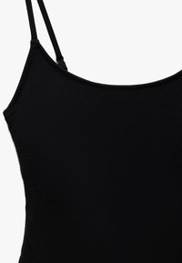 Haut sans manches noir avec de fines bretelles, présentant un tissu texturé et un décolleté arrondi. Design simple et minimaliste sans embellissements.