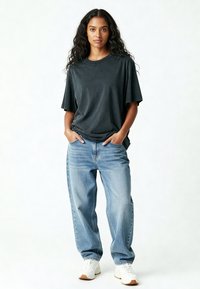Tricou oversized gri închis cu mâneci scurte, asociat cu blugi lejeri albaștri deschiși și adidași albi, având o croială relaxată și o textură moale.