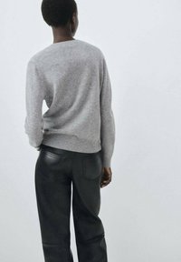 Suéter de lana gris con escote redondo, combinado con pantalones de cuero negros. Las texturas son suaves y lisas, mostrando detalles sutiles.