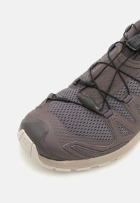 Grå sportskor med mesh-överkonstruktion, gummisul och snörning. Har texturerade accenter och en stödjande tåskydd.