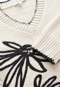 Pull en tricot crème avec un motif floral noir, col en V, col et poignets côtelés texturés avec couture contrastante.