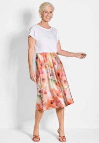 Top corto bianco a maniche corte con decorazioni abbinato a una maxi gonna floreale pastello con fiori sovradimensionati nelle tonalità di rosa e arancione.