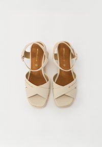 Beige kanvas sandaler med kryssede stropper, justerbar ankelspenne og såle i naturlig lær. Flat såle med subtil merking.