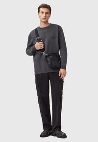 Grå sweatshirt med logo, sort crossbody taske, sorte cargo bukser og sorte sko. Tasken har tekstureret stof og justerbar rem.