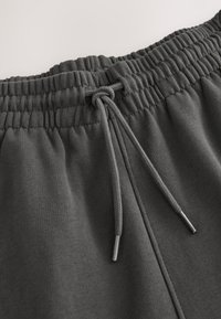 Ciemnoszare spodnie dresowe z teksturowanym pasem, wyposażone w ściągacz ze sznurkiem zakończonym metalowymi końcówkami oraz miękką, gładką tkaniną.