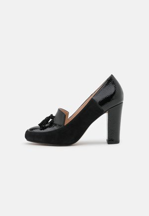 Czarny, lakierowany loafer na wysokim, masywnym obcasie z frędzlami z przodu, pokazany z profilu na jasnym tle.