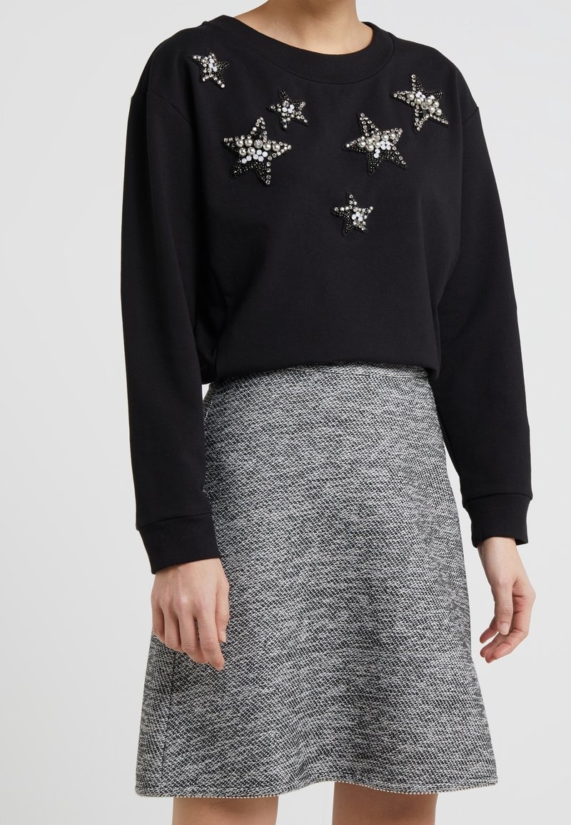 Sweatshirt nero con decorazioni a forma di stella e una gonna grigia svasata dal texture. Il sweatshirt presenta un collo a giro e maniche lunghe.