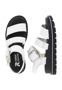 White sandals with three wide straps, a silver buckle, and a textured black sole. Features a contrasting white trim along the sole.
