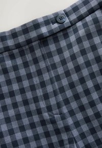 Grijs-zwart geruit stof met een gladde textuur, voorzien van een zichtbare donkere knoop in de tailleband en zijdelingse stiksel details.