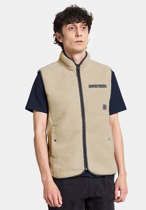 Beige Fleece-Weste mit hohem Kragen, Frontreißverschluss und einer Brusttasche. Mit dunklen Akzenten und einer weichen, strukturierten Oberfläche.
