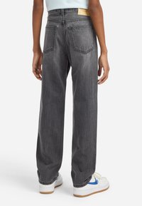 Jeans de pierna ancha grises, hechos de denim, con una cintura alta, dos bolsillos traseros y costuras minimalistas. Combinados con zapatillas blancas.