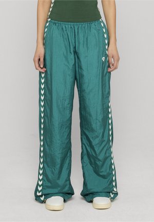 Turkis, letvægts og let skinnende træningsbukser med elastisk talje og hvide chevron detaljer på siden. Velegnet til afslappet brug.