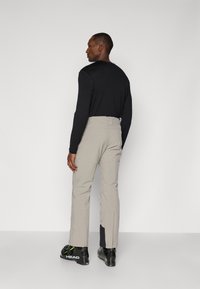 Pantaloni de schi bej cu un design ajustat, picioare inferioare cu fermoar și o curea. Purtați cu bocanci de schi negri cu accente verzi.