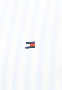 Το ύφασμα με λευκές ρίγες διαθέτει ένα μικρό κεντημένο λογότυπο με ναυτικό μπλε, κόκκινες και λευκές ορθογώνιες φιγούρες, στο κέντρο του υφάσματος.