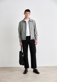 Light gray zip-up jacket with ribbed cuffs, white crew neck shirt, black wide-leg trousers, and black leather shoes. Holding a black bag.