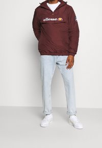 Viininpunainen huppari, jossa on vetoketjullinen rintatasku ja valkoinen logo. Yhdistetty vaalean sinisiin farkkuihin ja valkoisiin lenkkareihin.