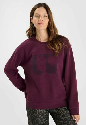 Maroon sweatshirt with long sleeves, crew neck, and a large dark graphic on the front. Soft texture with ribbed cuffs and hem.