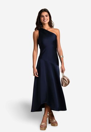 Vestido de satén marino con un diseño de un solo hombro, que presenta una silueta A-line fluida. Combinado con un bolso de mano bronce y tacones de plataforma dorados.