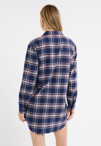 Abito camicia a quadri blu navy con maniche lunghe, dettagli bianchi e rossi, polsini con bottoni e orlo curvo. Tessuto morbido al tatto.