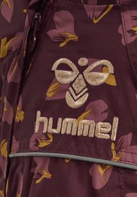 Burgundy jacka med blomsterdesign i lila och gult, med en broderad logotyp och dragkedja. Strukturerad tyg med silverdetaljer.