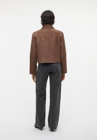 Brun rauh suede cropped jakke med krave, parret med højtaljede mørkegrå jeans, der viser en glat tekstur og en afslappet pasform.