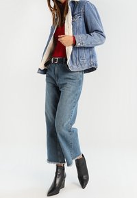 Jeansjacke mit einem mit Fleece gefütterten Kragen, rotes Oberteil, hoch taillierte blaue Jeans und schwarze Stiefeletten mit Absatz und spitzen Zehen.