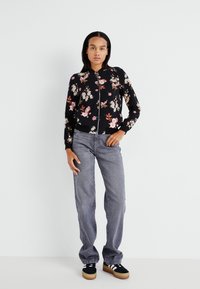 Veste bomber noire à motifs floraux avec des fleurs roses et blanches, poignets côtelés et fermeture éclair. Assortie à un jean large gris et des baskets noires.