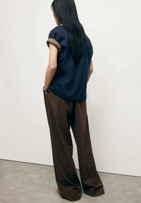 Marineblauw oversized t-shirt met omgeslagen mouwen, gecombineerd met bruine wijde broek. De stof lijkt zacht met een gladde textuur.