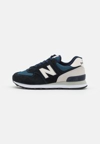 Marinblå och beige New Balance-sneaker med vit sula, mocka och mesh-paneler, samt snörning, visad från den laterala sidan.