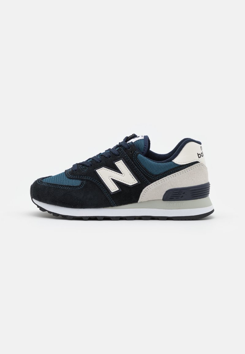 Marinblå och beige New Balance-sneaker med vit sula, mocka och mesh-paneler, samt snörning, visad från den laterala sidan.