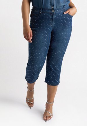 Pantaloni capri in denim scuro con pois bianchi, caratterizzati da una vita alta, tasche frontali e orlo risvoltato. Abbinati a sandali argentati.