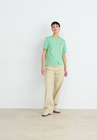 Camiseta de algodón verde claro con cuello redondo, combinada con pantalones anchos beige. El conjunto se complementa con zapatos plateados.