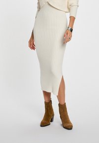 Gonna midi lavorata a maglia di colore crema con texture a coste e spacco laterale, abbinata a stivaletti alla caviglia in suede beige con tacco a blocco.