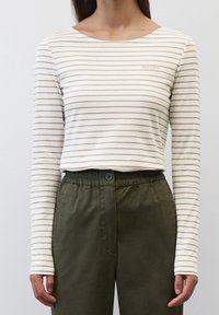 Langärmliges, gestreiftes Oberteil in Creme mit dünnen braunen Streifen, mit einem Boot-Ausschnitt und einem Logodetail auf der Brust. Kombiniert mit olivgrünen Hosen.