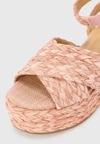 Sandale espadrille tressée rose avec une épaisse plateforme, présentant des sangles croisées et un motif texturé en damier sur la semelle.