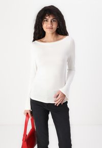 Long-sleeve white top made of soft fabric with a scoop neckline, paired with black jeans and a red handbag. Simple design with a smooth texture.