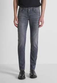 Jeans de mezclilla gris con corte slim, que presentan cinco bolsillos y un sutil detalle de desgastado. Llevados con botas negras hasta el tobillo.