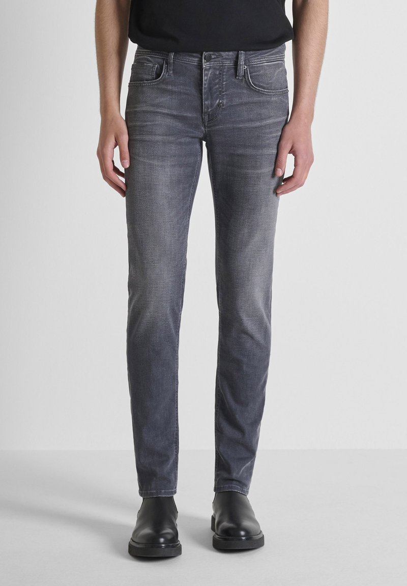 Jeans de mezclilla gris con corte slim, que presentan cinco bolsillos y un sutil detalle de desgastado. Llevados con botas negras hasta el tobillo.