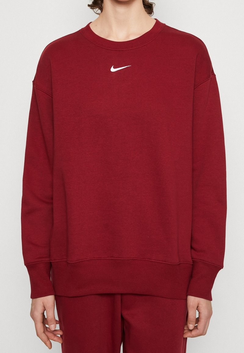 Sudadera marrón burdeos con cuello redondo, hombros caídos y dobladillo acanalado. Presenta un discreto logo blanco de Nike en el pecho. Textura suave.