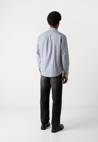 Csíkos, világoskék és fehér gombos ing, sötét, egyenes szárú nadrággal és fekete cipővel párosítva. Látható hátsó varrási részletek.