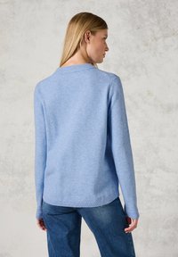 Hellblaues Strickpullover mit Rundhalsausschnitt, gerippten Bündchen und Saum sowie einem Schulterdesign mit落下, kombiniert mit dunkelblauen Jeans.