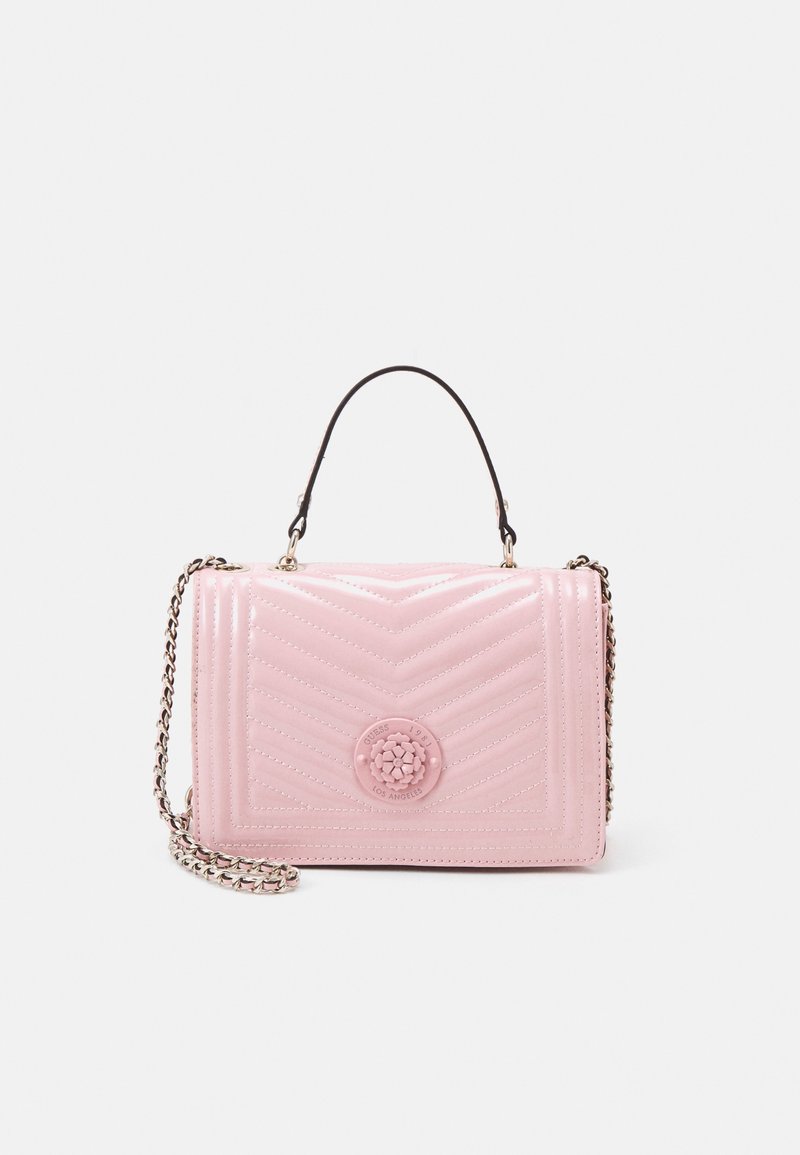 Sac à main matelassé rose clair avec piqûres en chevrons, anse supérieure noire, bandoulière chaîne argentée, et emblème rond à logo floral sur le rabat avant.