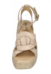 Beige suede espadrille wedge sandal with a knotted front design, adjustable ankle strap, and woven jute midsole. Flat sole with textured finish.
