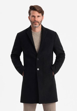 Abrigo de lana negro con cuello con muescas, diseño de un solo botón, dos bolsillos frontales y dos botones, llevado sobre un suéter de punto beige.