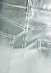 Jean métallisé argenté avec une texture lisse et réfléchissante. Présente des coutures visibles, des poches avant et arrière, et un design ajusté.