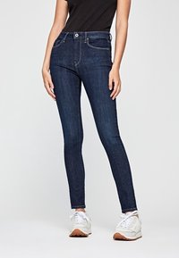 Hubené tmavě modré džíny s středně vysokým pasem, předními kapsami a kontrastním šitím, kombinované s bílými teniskami.