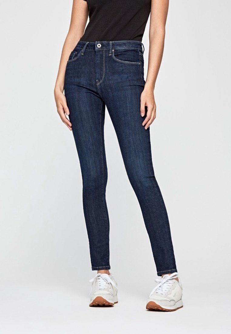 Hubené tmavě modré džíny s středně vysokým pasem, předními kapsami a kontrastním šitím, kombinované s bílými teniskami.