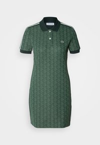 Robe polo manches courtes vert foncé avec motif géométrique, col à boutons, bandes latérales et petit logo crocodile sur la poitrine.